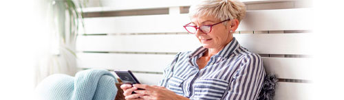 tech savvy older woman in casual clothes sitting outside reading her phone screen